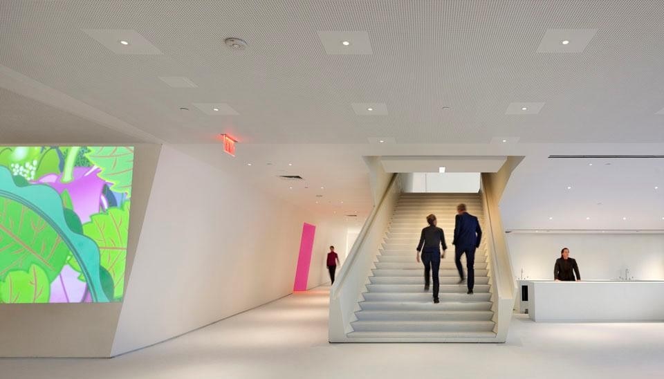 Behind the grand stair, the secondary screening room beckons through a pink vestibule. At left, a 15 m-long wall projection transforms a tilted wall into a screen. ©Peter Aaron. Courtesy of Museum of the Moving Image