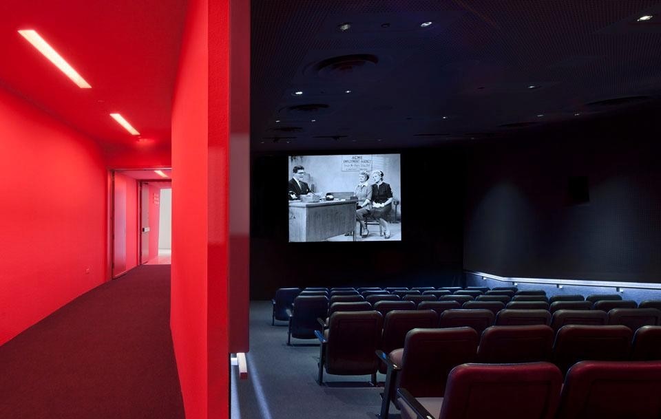 The 68-seat screening room, with exposed loudspeakers and perforated grey acoustical surface, accessed through a pink corridor. ©Peter Aaron. Courtesy of Museum of the Moving Image