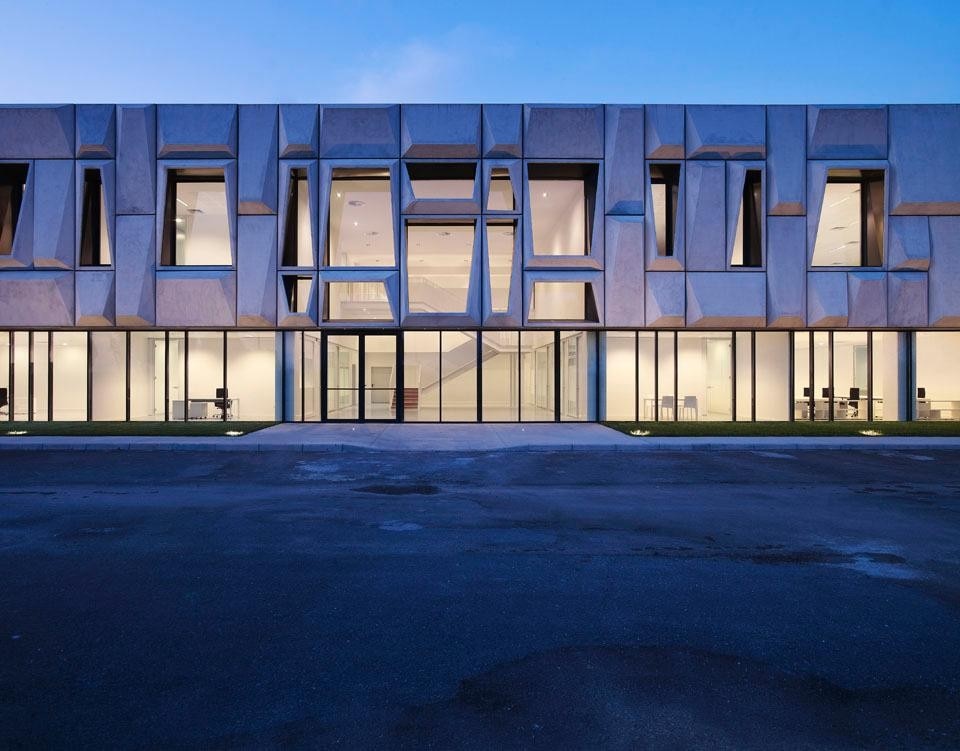 A three-dimensional tectonic façade rests on a transparent and light base letting the new headquarters for a clothing company in Nola’s industrial suburbs.