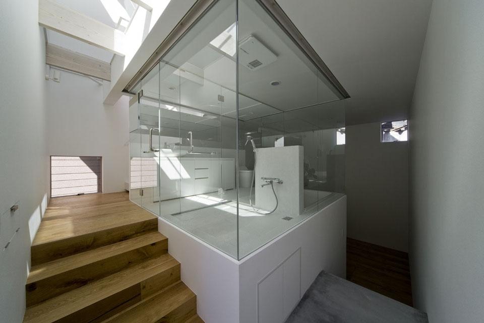 The bathroom and toilet are enclosed behind completely transparent glass and occupy an elevated central space on the ground floor.  