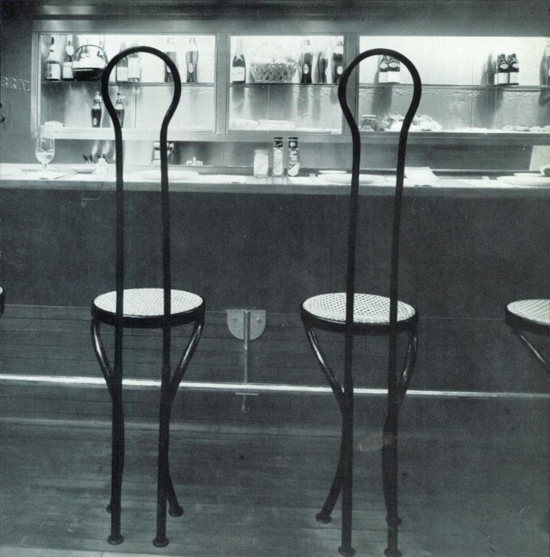Thonet-type chairs, in metal, do not swivel; the high backs protect guests them from passers-by. Elongation is playfully transferred from the legs to the back. 