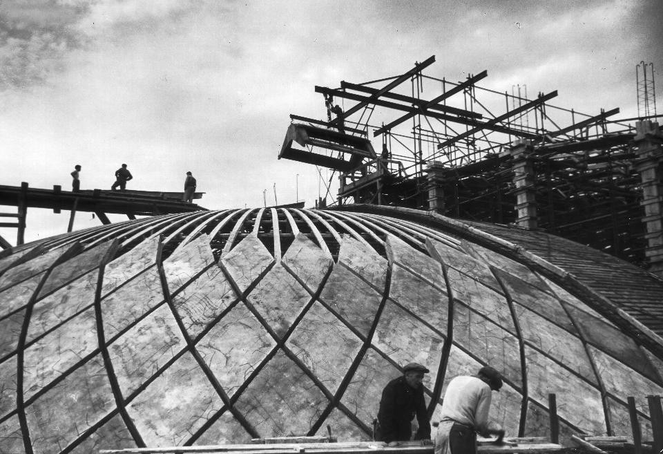 The roof of the hall during construction. Note the scale of human figures in the vast frame of the structure