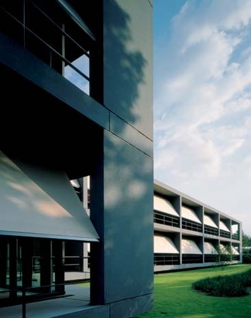 The modern, horizontal architecture’s large windows, are set back from a dark-grey concrete prefabricated external superstructure that embraces the building on all sides, serving as both a loggia and brise-soleil