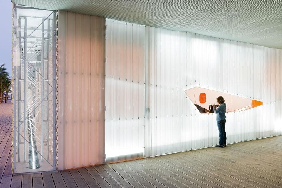 A broken line cuts out the
aperture of the reception
desk in the translucent lateral
front. In the foreground is the
metal frame of the facades,
wind-braced and clad with
retro-illuminated plastic pipes.