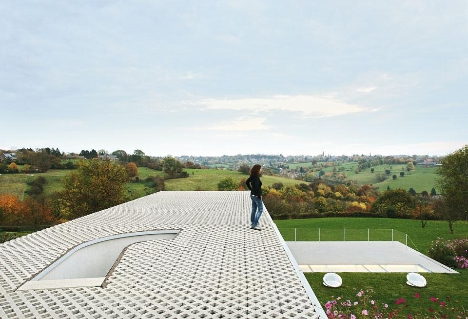 The facades and roof are
clad with prefabricated
concrete units, of the type
normally used to pave car
parks and that allow grass
to grow on them. In fact the
roof of the house can also
function as a car-parking
area. The concrete blocks
have been lab tested to
ensure vertical resistance
to compression. The house
echoes the landscape with
its distinctly horizontal
design, and Firket’s
historical reference was
Villa Malaparte, on the Isle
of Capri. In the intentionally
elemental construction
process, five simple materials
were chosen: concrete, car
park paving blocks, marine
plywood, steel and glass