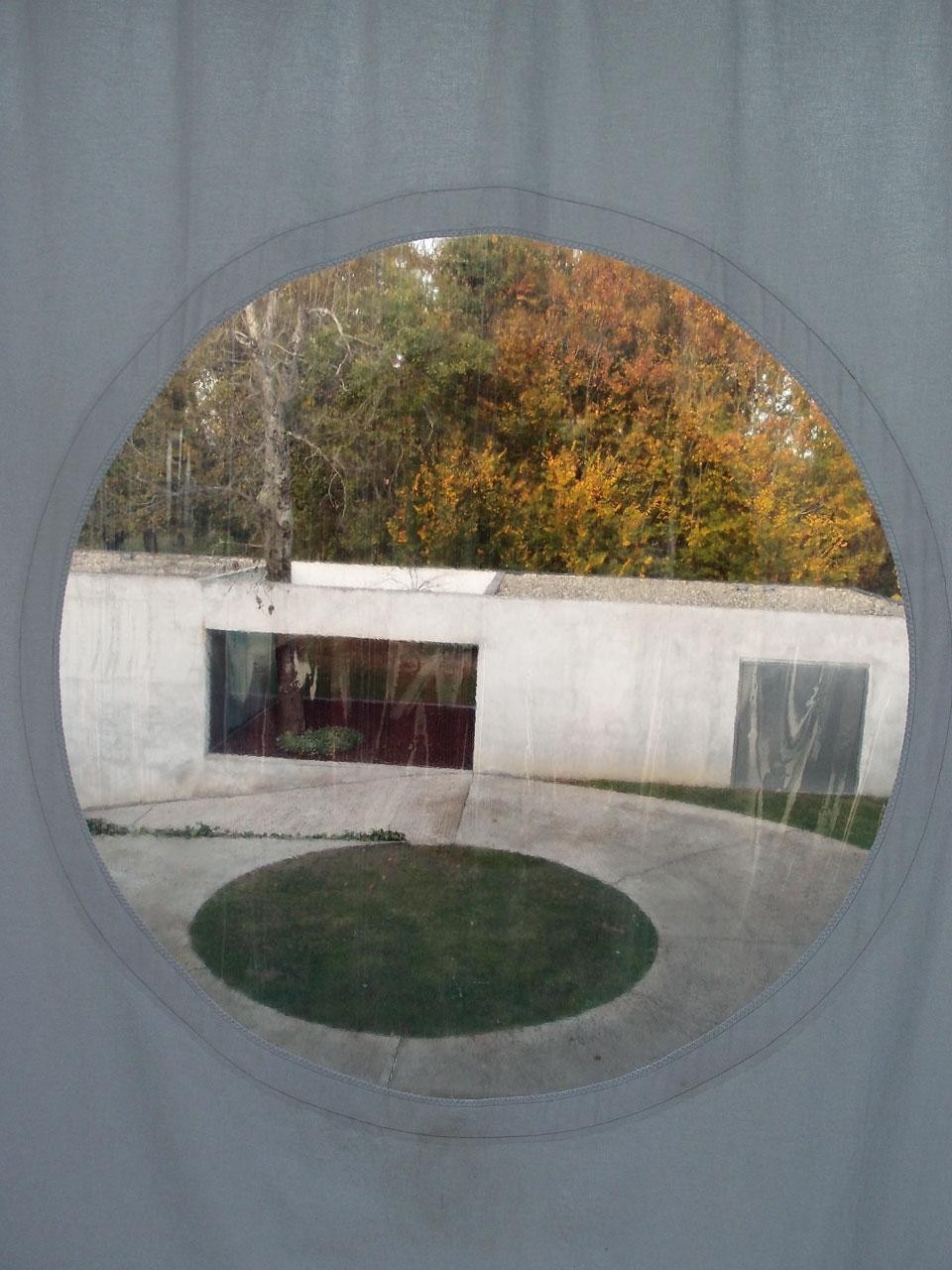 The <em>trompe l’oeil</em> effect of a
light cloth is heightened by
the fact that the fabric itself
contains a circular window in
which the view to the forest
appears as a picture — like
the darkness of the sea seen
through the porthole of a cosy
ship’s cabin
