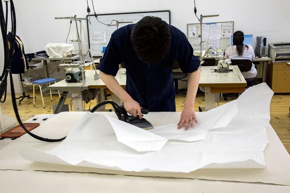 Top: The <em>In-Ei</em> Issey Miyake
lamps are developed with a
special fabric — a regenerated
fibre derived from pet bottles
and with a transparency
superior to that of paper —
which enables 3D forms to be
perfectly maintained without
any internal structure.
When not in use, the lamps
can be folded up for storage. Above: A phase of the cutting and presss-ironing process behind the making of <em>In-Ei</em>