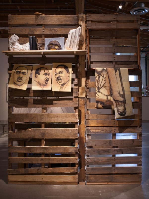 Edgar Arceneaux A Time to Break Silence: Reliquary of the Stars, 2014 Acrylic on satin, mounted on MDF on yardstick railing, found plaster relics from St. Anne's church in Detroit, 2 Bibles (1 prop, 1 real), 5 pieces of electronic motherboard, prosthetic rubber mask, wood frame, wood shelf, pallets Courtesy of the artist and Susanne Vielmetter Los Angeles Projects