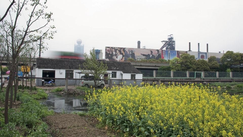 Star-Leader of the Village along the Highway. Huaxi is located within a dense network of rivers and
highways in the Yangtze River Delta. The Shanghai-Nanjing
Highway runs by the village; it takes 1-2 hours to reach
either of the cities. On a billboard that screens the polluting
industrial-scape from the highway, Wu Renbao, the 85-year old
leader of the village, smiles for the journalists with his son
Wu Xie’en, the future leader of the village