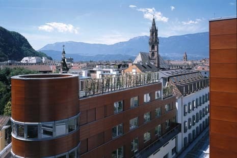 Il Greif Center nel contesto urbano con il campanile gotico della cattedrale sullo sfondo. L’ala con la torre circolare rivestita in legno ospita le abitazioni