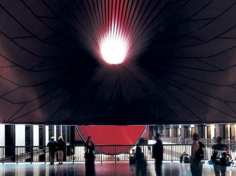 Con le sue dimensioni (150 metri di lunghezza) la scultura sembra ingoiare l’austera architettura di Herzog e de Meuron. L’opera di Kapoor si estende da un’estremità all’altra della Turbine Hall della Tate e abbraccia la passerella pedonale.
