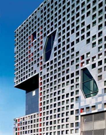 In facciata gli arretramenti di piano sono evidenziati da un trattamento compositivo e cromatico diverso dalla superficie più esterna. Bucature irregolari interrompono la serialità della perforazione dei fronti