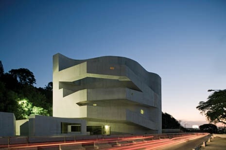 Impostato su una piattaforma sopraelevata rispetto al piano stradale, 
il prisma di cemento bianco, quasi totalmente 
privo di aperture, si inserisce tra un promontorio ricco di vegetazione 
e un asse a forte percorrenza lungo il fiume