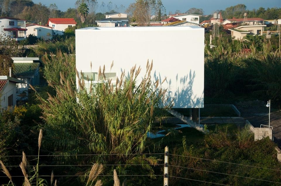 Il volume bianco, compatto e geometrico dell'edificio si staglia nel contesto delle case di tipologia tradizionale