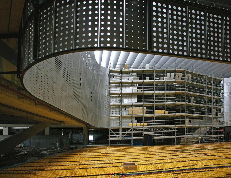 Interno della corte centrale: montaggio dei pannelli forati in alluminio sulla struttura metallica. La struttura è appesa alle travi reticolari della copertura, che funzionano anche come schermatura dello spazio all’irraggiamento solare.
