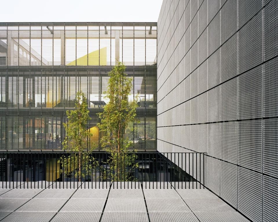 Camera di Commercio, Kortrijk, Belgio. L’edificio possiede una natura duale: verso la strada presenta un <i>curtain wall</i> vetrato, mentre il prospetto sulla corte interna è protetto dal sole grazie a una tessitura metallica