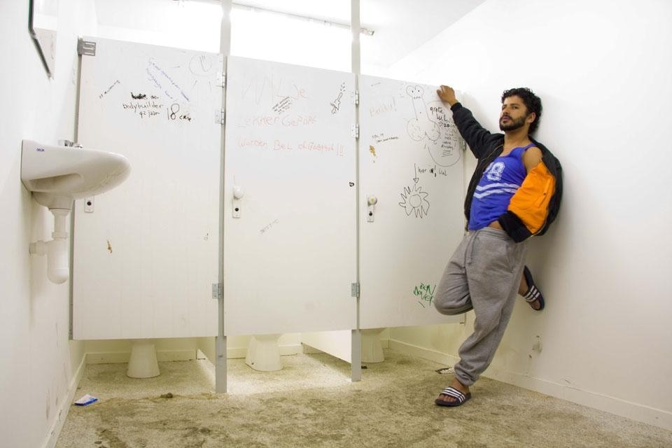 Bagni pubblici nello spazio di fronte alla ruota panoramica, accanto a una limousine bianca che amplifica i contrasti presenti nell'intero sito. 