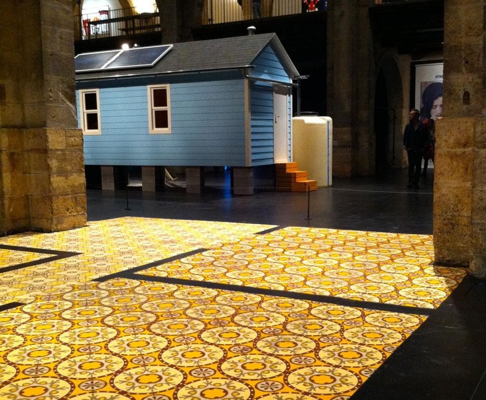 Foto di apertura: il progetto <i>La maison sur l'eau</i> del collettivo Ici est Ailleurs
è la proposta di una soluzione per la crescita urbana attraverso la realizzazione di un quartiere di fattorie galleggianti. Qui sopra: sullo sfondo, la casa di la casa di New Orleans di marjetica Potrc. In primo piano, Laurent Mareschal, <i>Beiti—My Home</i>, 2011, pavimentazione in ceramica fatto di una serie di spezie (curcuma, zenzero, zahtar, sommacco e pepe bianco)