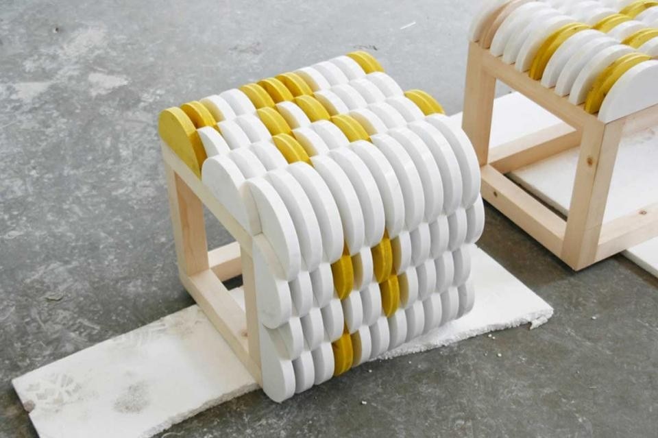 Il pouf realizzato in marmo Bianco Lasa, legno di faggio naturale e legno tinto giallo fluo.