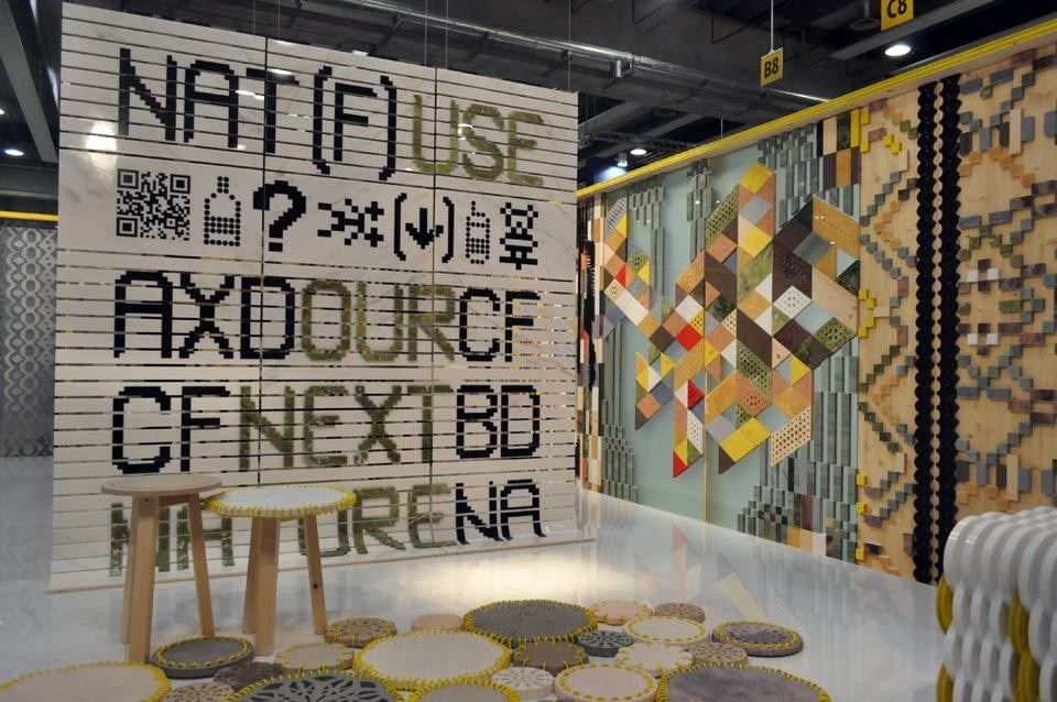 Panca e pouf sono realizzati in marmo Bianco Lasa, legno di faggio naturale e legno tinto giallo fluo. La struttura di sostegno è in legno di faggio naturale.  A terra, il tappeto lapideo composto da cerchi in marmo tenuti insieme da un cordone giallo.