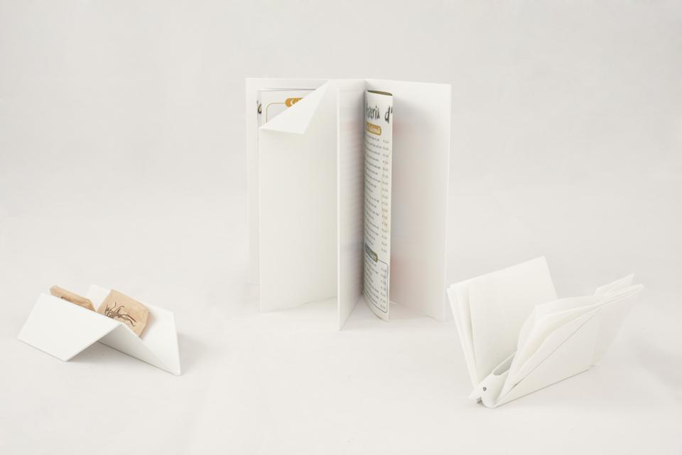 Apparecchiare la città di studio Ghigos ideas: paper. Un aeroplanino porta-bustine di zucchero e un uccellino portatovaglioli
sembrano fermarsi quasi per caso sul tavolo, mentre un
libro aperto con orecchio-promemoria cattura tra le sue pagine il
menu del giorno. Produzione: Metallurgica Motta