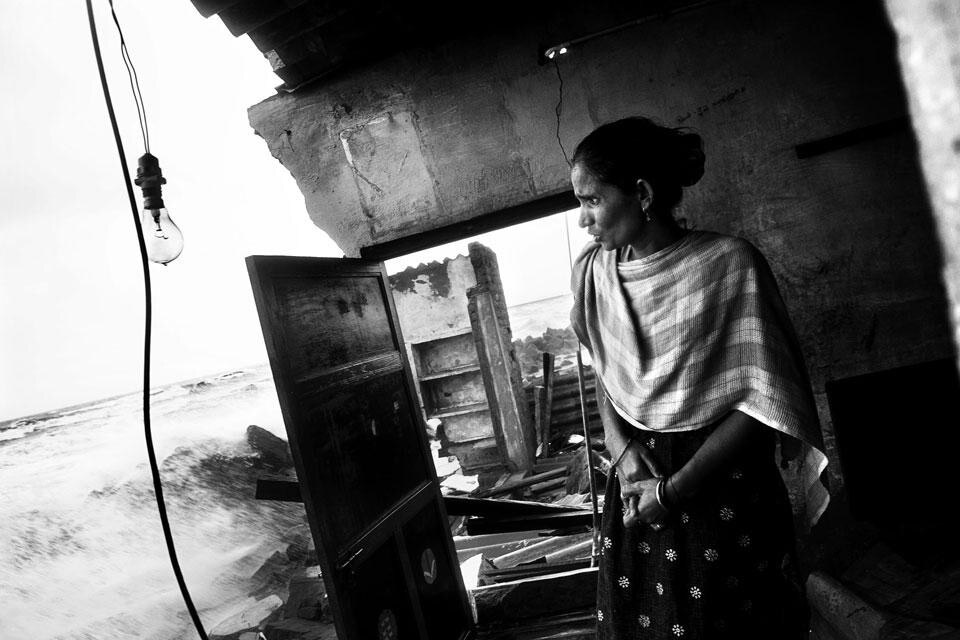 Ennore, Tamil Nadu, India. Il mare è estremamente violento in questa zona. Una donna guarda il mare agitato dalla sua casa in parte distrutta. Nonostante le barriere, ogni monsone, le acque diventano violente e si mangiano edifici e parti di terraferma
